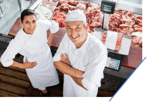 two butchers standing in front of a glass container full of their meat products.